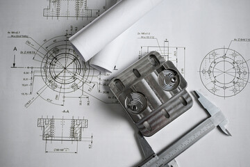 Metal machined part being measured with a caliper, placed on top of engineering blueprints