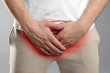 STD (sexually transmitted diseases). Man holding hands near his groin on grey background, closeup