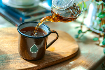 Freshly brewed tea is gently pouring into a rustic mug, creating a perfect afternoon setup