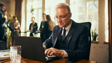 Focused senior businessman typing on laptop during professional networking event, showing dedication and efficiency. Developing strategy and preparing for consultation. Business, achievement concept