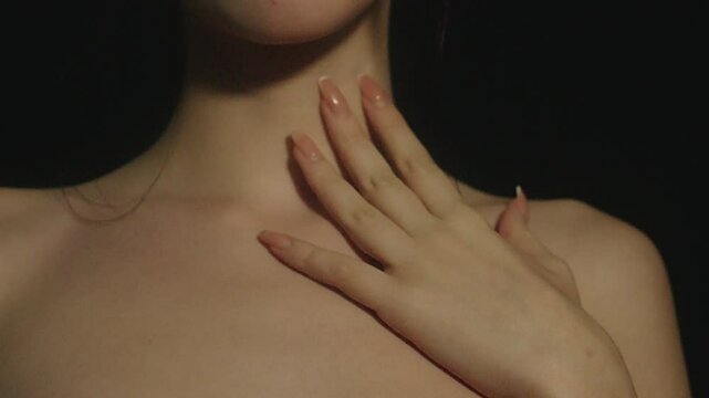 Closeup of a young and sexy teenage girl slowly passing her long nails hands over her neck and  breast in a sensual environment and black background