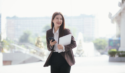 Confident Asian businesswoman standing on a busy city street with a smartphone in her hand, stylish and professional, representing the modern entrepreneur.