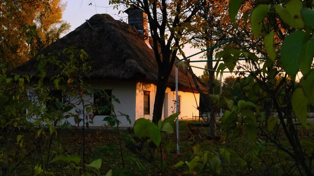 Rustic Ukrainian Cottage with Thatched Roof in Lush Green Surroundings at Sunset