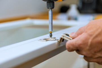 Contractor is securing hardware to white door using screwdriver in installing door hinges workshop