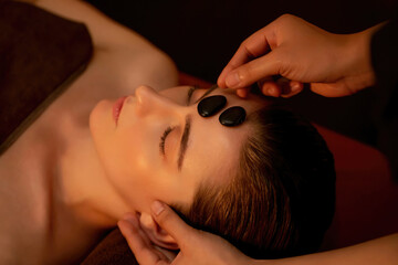 Caucasian woman enjoying relaxing anti-stress head massage with hot stone and pampering facial...