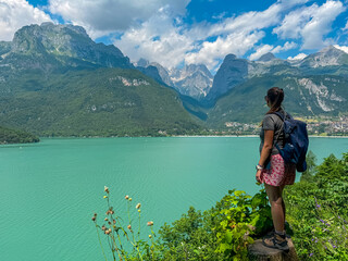 Hiker woman looks at alpine retreat village at idyllic mountain lake Lago di Molveno. Scenic view of majestic mountains Brenta Dolomites, National Park Adamello Brenta, Trentino, Italy. Wanderlust