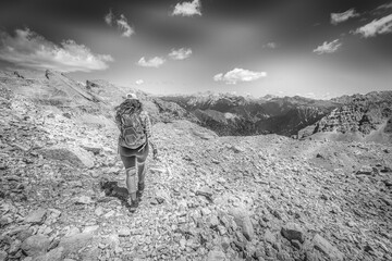 Young woman with hair blowing in the wind hiking outdoors in dolomite mountains. Mount Latemar, Trentino, Italy. Traveling concept photography and outdoor sport activity. Black and white photo