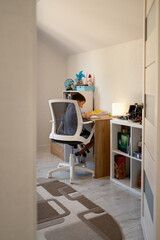 A young boy is diligently doing his homework at a desk in a modern, cozy study room. The setting is well-organized and inviting, creating an ideal environment for learning and concentration.