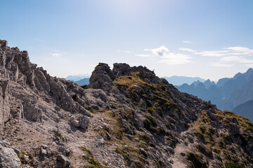 Hiking trail along remains of defensive line first world war on top of Jof di Miezegnot. Surrounded by majestic ridges of Julian Alps shrouded in misty haze, Friuli Venezia Giulia, Italy. Wanderlust