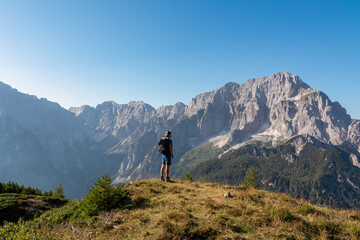 Obraz premium Active hiker man on alpine meadow with scenic view of rugged mountain peak Jof di Montasio. Majestic ridges of Julian Alps in Somdogna, Friuli Venezia Giulia, Italy. Wanderlust Italian Alps in summer