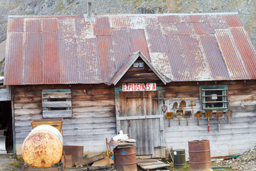 Rustic wooden cabin with a rusted tin roof and weathered barrels in front.