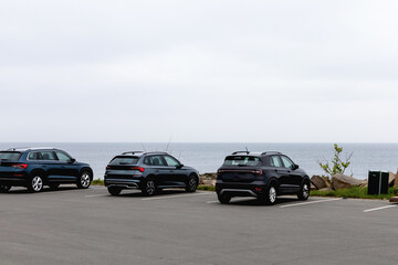 Obraz premium Parked cars on the seashore. Rocky seashore and houses in cloudy weather.