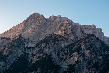 Scenic view of stunning mountain peak Jof Fuart bathed in soft glow of twilight. Massive rugged ridges of majestic Julian Alps seen from Val Saisera, Valbruna, Friuli Venezia Giulia, Italy. Sunrise