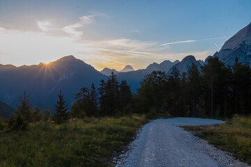 Hiking trail with sunrise view of silhouette of majestic mountain peaks of Julian Alps, Friuli Venezia Giulia, Italy, Europe. Veil of mist in alpine wilderness. Gentle twilight in Italian Alps. Hike