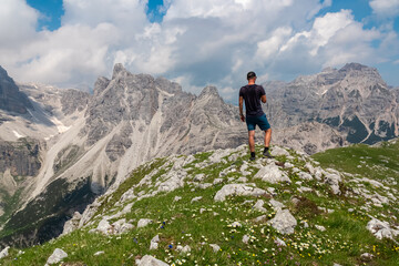 Fototapeta premium Hiker man on top of Cima Sophia with panoramic view of majestic cloud covered rugged mountain peaks of Brenta Dolomites, Trentino, Italy. Summer wanderlust in alpine wilderness Italian Alps. Freedom