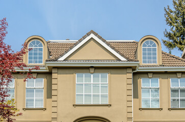 Top of grey stucco luxury house with shingle roof, red and yellow trees and nice windows in Summer in Vancouver, Canada, North America. Day time on June 2024.