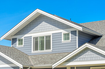 Top of grey stucco luxury house with shingle roof, red and yellow trees and nice windows in Summer in Vancouver, Canada, North America. Day time on June 2024.