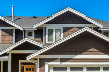 Top of grey stucco luxury house with shingle roof, red and yellow trees and nice windows in Summer in Vancouver, Canada, North America. Day time on June 2024.