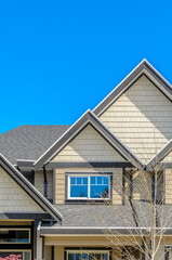 Top of grey stucco luxury house with shingle roof, red and yellow trees and nice windows in Summer in Vancouver, Canada, North America. Day time on June 2024.