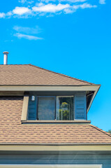 Top of grey stucco luxury house with shingle roof, red and yellow trees and nice windows in Summer in Vancouver, Canada, North America. Day time on June 2024.