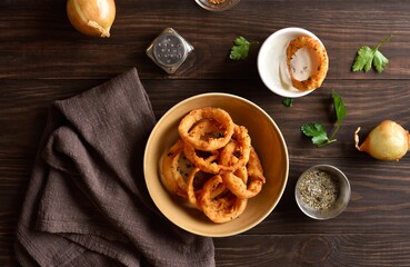 Crispy fried onion rings in bowl on wooden table