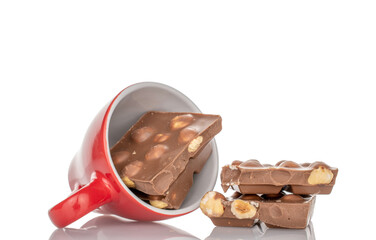 One bar of dark chocolate with hazelnuts in a ceramic dish, close-up, isolated on a white background.