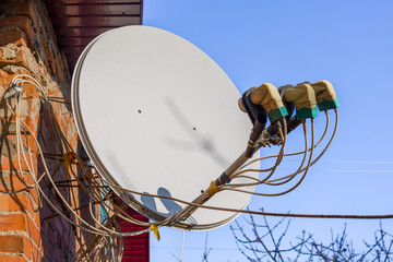 Satellite dish mounted on a brick wall against a clear blue sky. Multiple cables connect to the receiver.