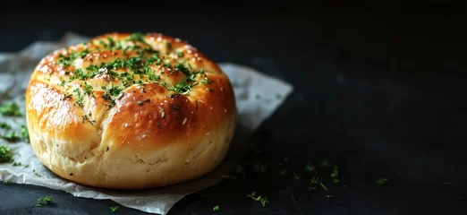 Selbstklebende Fototapeten Freshly baked bread topped with herbs, golden crust, soft interior, placed on parchment paper, dark background, copy space for text © Vergiliy