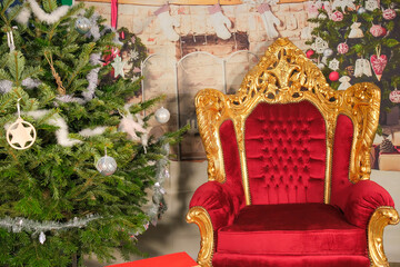 View of a red and golden colour Santa Claus armchair, next to a decorated Christmas tree