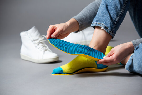 Close up of female hands holding blue orthopedic insoles, white sneakers on a gray background .
