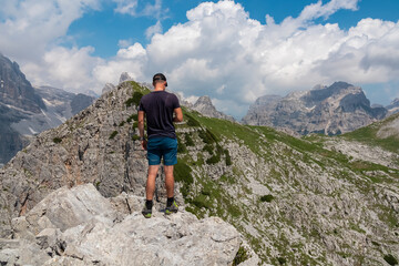 Hiker man on top of Croz dell'Altissimo with panoramic view of majestic cloud covered rugged mountain peaks of Brenta Dolomites, Trentino, Italy. Summer wanderlust in alpine wilderness Italian Alps