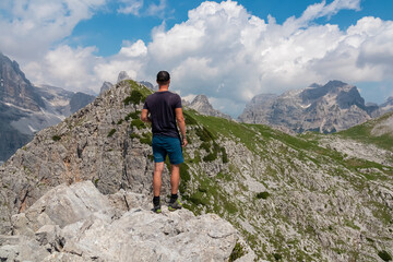 Fototapeta premium Hiker man on top of Croz dell'Altissimo with panoramic view of majestic cloud covered rugged mountain peaks of Brenta Dolomites, Trentino, Italy. Summer wanderlust in alpine wilderness Italian Alps