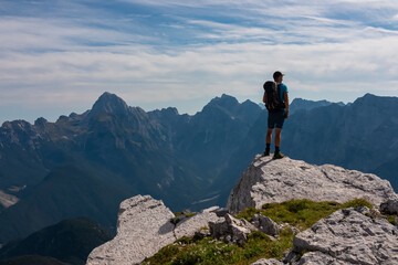 Hiker man on top of mount Cima Del Lago overlooking majestic mountain ridges ofJulian Alps, Italy Slovenia. Climbing on rocky summit in Triglav National Park. Alpine wilderness in summer. Wanderlust
