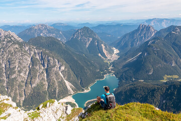 Hiker man on top of Cima Del Lago with aerial view of alpine lake Lago Del Predil in Val Canale...