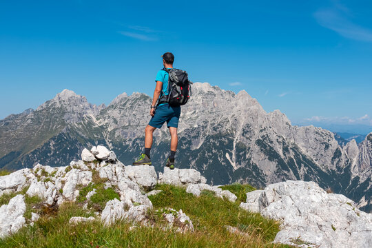Hiker man overlooking pristine rugged mountain peaks of Western Julian Alps, Italy, Europe. Wild hiking trail along majestic ridges in Triglav National Park. Wanderlust in alpine wilderness in summer