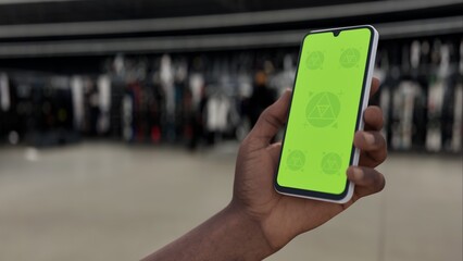GREEN SCREEN CHROMA KEY A person holding a smartphone in a sports goods store with a green screen for mockups, retail, or shopping app interfaces