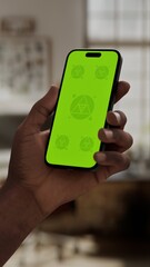 GREEN SCREEN CHROMA KEY A hand holding a smartphone with a green screen in a cozy home environment with natural daylight and a modern interior