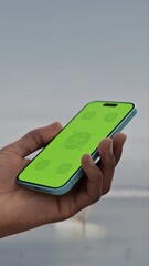 GREEN SCREEN CHROMA KEY A person interacts with a smartphone on a beach with a green screen, ideal for app mockups or digital interface overlays. Peaceful beach setting