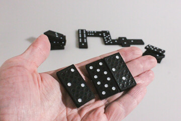 Black domino figures lie ready for play on a white background. First move, two teams. Figures in the player's hand. Board games. Family entertainment. Excitement. Victory. Poster and background