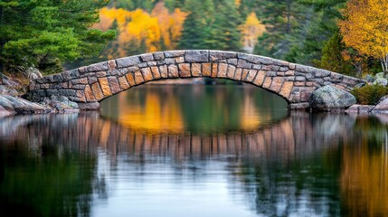 Fototapeta premium Tranquil Stone Arch Bridge Reflecting Autumn Colors in Serene Lake Surrounded by Vibrant Trees with Golden Leaves and Calm Waters in a Scenic Nature Setting