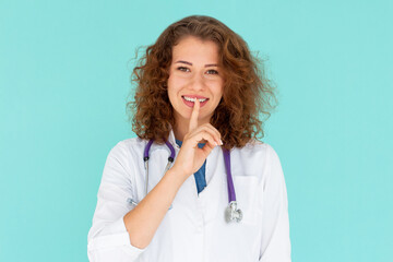 Mature woman doctor holding finger to lips in a shushing gesture, isolated over a blue background.