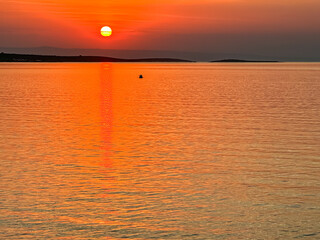 Breathtaking fiery sunset over calm Adriatic Mediterranean Sea in Premantura, Istria peninsula, Croatia, Europe. Reflection of the sun on water creates shimmering path that extends towards horizon