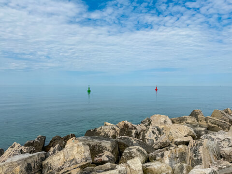 Two navigational buoys marking the channel for safe passage in the harbor of coastal town Umag, Istria peninsula, Croatia, Europe. Large rocks form breakwater towards Adriatic Mediterranean sea