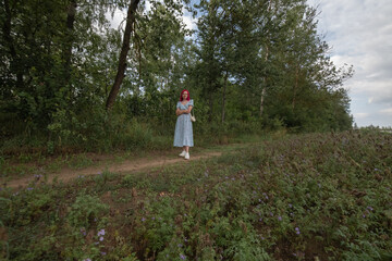 Young beautiful girl with red hair in nature in a beautiful summer dress.