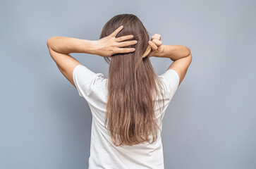 Fototapeta premium Combing long hair. Woman in white t-shirt. Hands behind head. Rear view on gray background isolated.