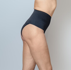 Naked female body in black postpartum panties on gray background. Body positive concept, Side view.