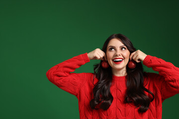 Happy woman trying Christmas balls as earrings on green background, space for text