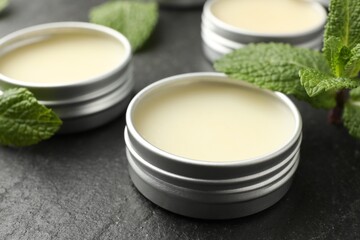 Mint lip balms and green leaves on black table, closeup. Cosmetic product