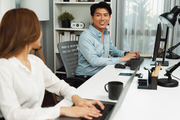 Fototapeta premium Smiling Asian man talking with woman colleague in planning marketing report project on laptop casual day while searching database on working desk at modern home office at side view image. Infobahn.