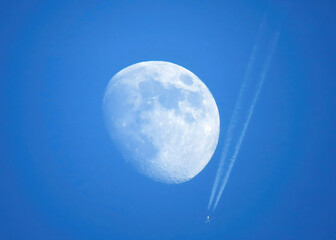 Moon against blue sky with jet streaking by. 